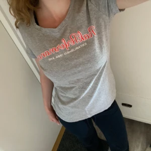 Grå t-shirt från Peak Performance - Säljer en grå t-shirt från Peak Performance med tryckt logga i orange och vitt på bröstet. Jättefint skick och nästan aldrig använd men tyvärr en märkning i nacken (sista bild) men inget som syns och som har gått igenom tyget! Pris kan diskuteras. Storlek m men passar också mig som är s/xs. Skriv om mer bilder eller frågor uppstår!🫶