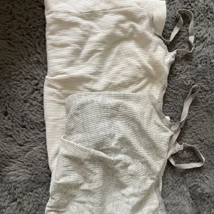 Två ribbade klänningar med smala axelband - Säljer två ribbade klänningar med smala axelband, en i ljusgrått och en i vitt. Båda har en enkel, rak passform och är tillverkade i mjukt, stretchigt material. Perfekta för varma dagar eller som ett bekvämt basplagg. 30 kr för både.