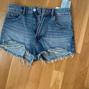 Blå jeansshorts med fransar från ZARA - Säljer ett par klassiska blå jeansshorts från ZARA med råa fransade kanter och femficksmodell. Shortsen har hög midja och en avslappnad passform. Perfekta för sommaren och enkla att matcha med allt. Jag har sytt de för hand lite vid rumpan för att de inte skulle vara så utsvängda där, man kan spretta upp de om man vill de är i storlek 38 men mer som 36 och de är högmidjade😊💗