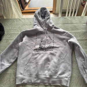 Lila hoodie från OBEY med tryck - Säljer en lila hoodie från OBEY med svart tryck framtill och texten 'The world is yours.' Tröjan har huva med dragsko och en stor magficka. Perfekt för dig som gillar streetwear och vill ha något bekvämt och stilrent.