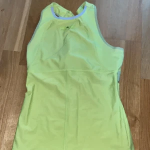 Gul/ grön linnetopp från Adidas Stella McCartney - Snygg gul/ grön linnetopp från Adidas Stella McCartney med sportig design och meshdetaljer upptill. Perfekt för träning med sitt lätta och ventilerande material. Brottarrygg och elastisk kant för extra komfort. Är barnstorlek 170 men är som en XS. 