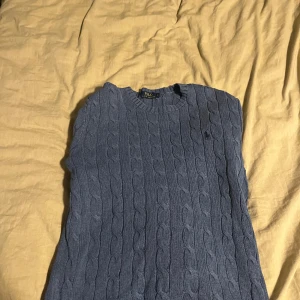 Blå kabelstickad tröja från Polo Ralph Lauren - Säljer en klassisk blå kabelstickad tröja från Polo Ralph Lauren. Tröjan har rund halsringning och långa ärmar, perfekt för lager-på-lager. Diskret broderad logga på bröstet. Superfin till både jeans och kjol!