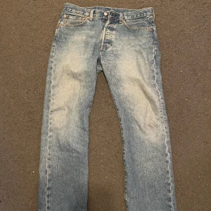 Levi's 501 blå jeans W31 L30 - Klassiska blå Levi's 501 jeans med raka ben och knappgylf. Jeansen har en tidlös tvätt och är tillverkade i robust denim. Passar perfekt för dig som gillar en ikonisk och avslappnad stil.