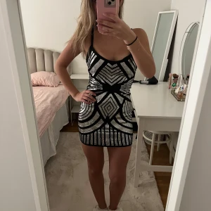 Svart och silver glittrig kortklänning - Säljer en snygg kort klänning i svart och silver med glittrigt geometriskt mönster. Klänningen är tight och ärmlös med djup urringning och smala axelband. Perfekt för tema fest