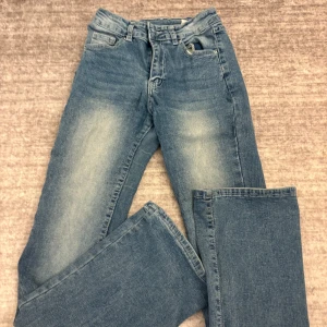 Blå jeans med broderade bakfickor - Säljer ett par klassiska blå jeans med snygga broderade detaljer och knappar på bakfickorna. Jeansen har en bootcut passform och är tillverkade i denim. Perfekta för dig som gillar en tidlös stil med lite extra detaljer.