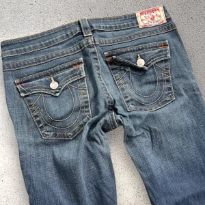Blå bootcut jeans från True Religion - Säljer ett par klassiska blå jeans från True Religion med bootcut-passform. Står storlek L men små i storleken då midjemåttet är 42cm rakt över!