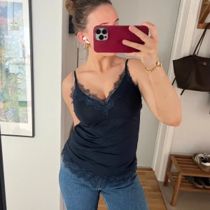 Mörkblå linnetopp med spets från Rosemunde - Supersnygg mörkblå linnetopp från Rosemunde med fina spetsdetaljer vid halsringning och nederkant. Tunn och mjuk, perfekt att styla till jeans eller kjol. Justerbara axelband för bästa passform.