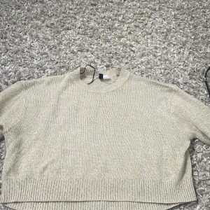 Beige stickad croppad tröja från H&M Divided - Säljer en beige stickad croppad tröja från H&M Divided. Tröjan har rund halsringning och långa ärmar. Perfekt att styla med höga jeans eller kjol för en avslappnad look.