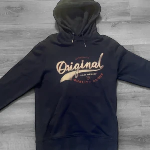 Mörkblå hoodie från Produkt med tryck - Säljer en mörkblå hoodie från Produkt med trycket 'Original Raw Denim Quality Goods' i beige och rött framtill. Klassisk huva med dragsko och magficka. Perfekt för en avslappnad stil. Storlek S! Hör av dig vid funderingar🙌