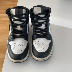 Nike Air Jordans svartvita sneakers - Säljer ett par klassiska Nike Air Jordans i svart och vitt. Skorna har hög modell, svart snörning och vit tå med perforeringar. Swoosh-logga på sidan och svartvit yttersula. Perfekta för dig som gillar streetstyle och vill ha en ikonisk sneaker.
