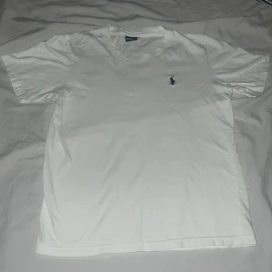 Vit t-shirt från Ralph Lauren med broderad logga - Klassisk vit t-shirt från Ralph Lauren med liten blå broderad logga på bröstet. T-shirten har rund hals och korta ärmar, perfekt för en clean och stilren look. Riktigt snygg till sommaren och är helt ny. Skick 10/10🌟🌟