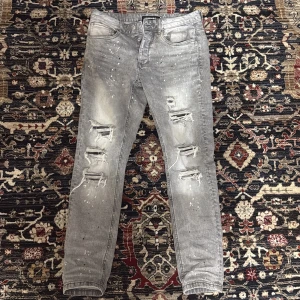 Grå slitna jeans från Lorenzo - Säljer ett par grå jeans från Lorenzo med slitningar och hål på framsidan. Byxorna har skinny passform och klassisk femficksdesign. Snygga detaljer med spräckliga effekter och dragkedja i gylfen.