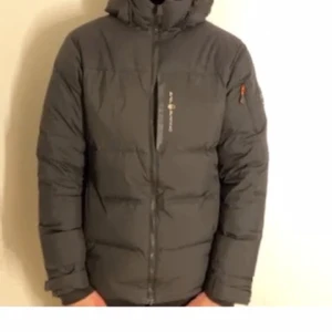 Svart dunjacka från sail racing  - Säljer en svart dunjacka från sail racing  med huva och dragkedja framtill. Jackan har lång ärm och diskret logga på bröstet samt ärmen. Perfekt för kyliga dagar.  Säljer den för lågt pris eftersom det är för liten 