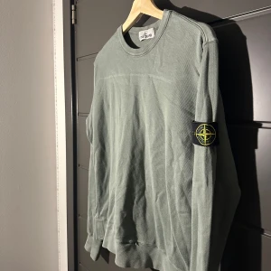 Oliv grön sweatshirt från Stone Island - Säljer en stilren grå sweatshirt från Stone Island med klassisk patch på vänster ärm. Tröjan har rund halsringning och långa ärmar. Perfekt för en avslappnad och trendig look. Som ni ser så är tröjan förstor på mig vid armarna och lite lång, men denna tröja blir perfekt till dig som är runt 170-175. Hör av er om ni har några frågor.