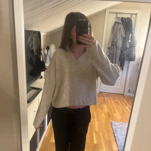 Beige ribbad stickad tröja - Mysig beige stickad tröja med v-ringning och ribbad struktur. Tröjan har långa ärmar och en lite oversized passform, perfekt för lager på lager under kyliga dagar.