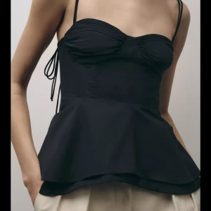 Svart trendig topp från Zara!!! Använd 1 gång!💞 - Trendig svart linnetopp med peplumskärning och tunna axelband. Toppen har rynkade detaljer vid bysten och knytning i sidan för en justerbar passform. Perfekt för en stilren och modern look.