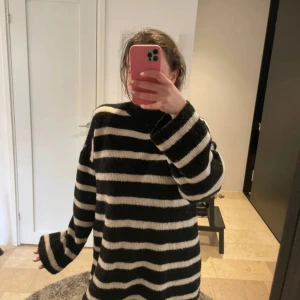 Svartvit randig stickad klänning - Mysig oversized stickad klänning med breda svarta och vita ränder. Klänningen har lång ärm, hög hals och är tillverkad i ett mjukt material. Perfekt för kyligare dagar och ger en avslappnad look.