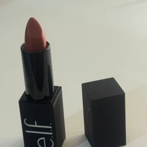 e.l.f. O Face Satin Lipstick i nyansen Vocal - Snyggt läppstift från e.l.f. i färgen Vocal, en varm nude-rosa ton med satin-finish. Kommer i en stilren svart hylsa med magnetlock. Perfekt för dig som vill ha en mjuk och krämig känsla på läpparna. finns 2 stycken av samma färg 