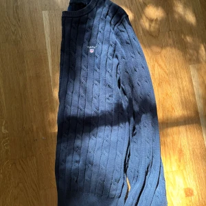 Mörkblå kabelstickad tröja från Gant - Säljer en superfin mörkblå kabelstickad tröja från Gant med rund halsringning och logga på bröstet. Perfekt för lager-på-lager-stil!