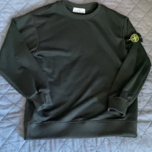 Svart sweatshirt från Stone Island - Säljer en svart sweatshirt från Stone Island med klassisk rund hals och lång ärm. Tröjan har den ikoniska Stone Island-loggan på vänster ärm. Perfekt för en stilren och avslappnad look.