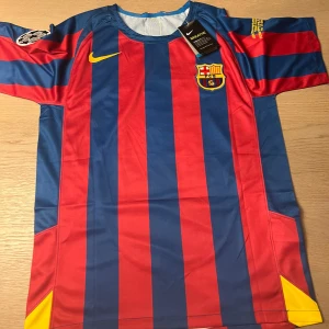 FC Barcelona fotbollströja Ronaldinho #10 - Säljer en klassisk FC Barcelona fotbollströja från Nike med Ronaldinho och nummer 10 på ryggen. Tröjan är blå och röd med gula detaljer, kortärmad och har klubbmärket på bröstet samt Champions League-märke på ärmen.