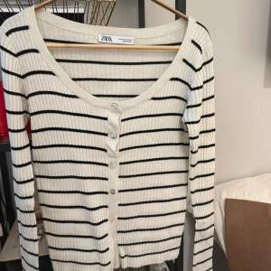 Randig ribbad kofta från Zara - Säljer en vit ribbad kofta från Zara med svarta ränder. Koftan har långa ärmar, knappar framtill och en smickrande, något djupare ringning. Perfekt att slänga över en topp eller bära som den är. Passar även mig som är en storlek S. Knappt buren.