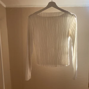 Vit långärmad mesh topp med vågigt mönster - Säljer en vit långärmad mesh topp med transparent material och vågigt mönster. Toppen har en rund halsringning och är figurnära i modellen. Perfekt att styla lager på lager eller som statement-plagg.