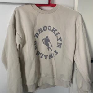 Beige sweatshirt från Gina Tricot - Säljer en beige sweatshirt från Gina Tricot med tryck 'Brooklyn Finals 85' . Tröjan har rund halsringning, långa ärmar och ribbade muddar vid ärmslut och nederkant.