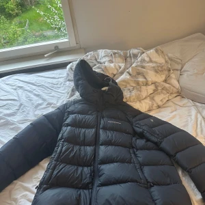 Mörkblå jacka från Peak Performance - Säljer en mörkblå jacka från Peak Performance i storlek XL. Jackan har huva och klassisk pufferdesign med breda kanaler. Perfekt för kyliga dagar och håller dig varm hela vintern. Snygg och stilren modell. Har som tjej använt den men ser ut som tjej och kill jacka!