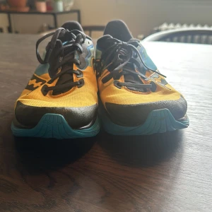 Saucony Ride löparskor i blått och gult - Säljer ett par Saucony Ride löparskor med snygg färgkombination i blått, gult och rött. Skorna har svarta snören, platt sula och rund tå. Perfekta för löpning och träning.