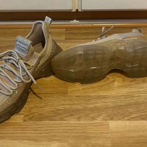 Steve Madden - Maxilla-R Sneakers Blush - Säljer ett par snygga beige sneakers från Steve Madden, modell Maxilla R. Skorna har stickad ovandel, glittriga detaljer på sidorna och tjock genomskinlig sula. Perfekta för dig som gillar trendiga och bekväma skor med extra bling. Helt nya och oanvända. Har inte kvar kvitto eller kartong.