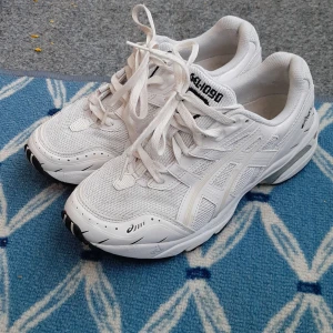 Vita Asics GEL sneakers - Säljer ett par fräscha vita Asics GEL sneakers med klassisk design. Skorna har snörning, rund tå och platt sula. Ovandelen är i mesh och syntetmaterial för bra andningsförmåga och komfort. Perfekta för träning eller vardagsstil.