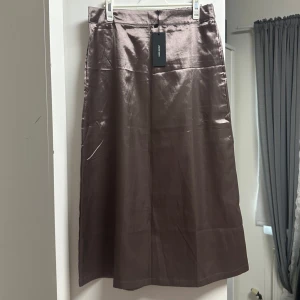 Satin kjol från Vero Moda - Säljer en glansig långkjol i satin i färgen fossil från Vero Moda. Oanvänd med etikett på. 