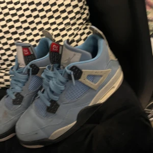 Nike Air Jordan 4 University Blue - Säljer ett par Nike Air Jordan 4 University Blue sneakers. Skorna är ljusblå med grå och svarta detaljer, meshpaneler och klassisk snörning. Ikonisk Jumpman-logga på plösen och sula med bra grepp. Perfekta för dig som gillar streetwear och sneakers.