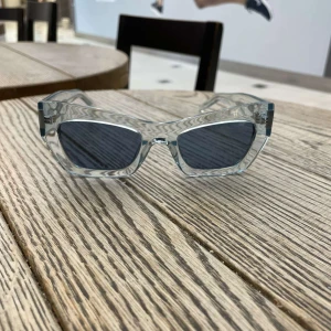 Boss HELT NY solglasögon  - Snygga solglasögon från BOSS med transparent, ljusblå båge och mörka glas. Rektangulär form som ger en modern och cool look. Perfekt accessoar för att lyfta din stil.
