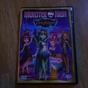 Monster High: 13 önskningar - Monster High: 13 önskningar är en animerad film på DVD där karaktärerna från Monster High hamnar i ett magiskt äventyr med önskningar och mystik. Omslaget är färgglatt med flera av de ikoniska Monster High-figurerna i centrum.