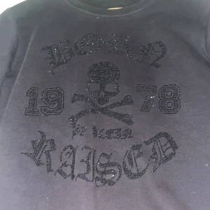 Svart sweatshirt från Philipp Plein Junior med dödskalle MÖTS UPP I GBG  - Cool svart sweatshirt från Philipp Plein Junior med glittrande dödskalle och texten 'Born Raised 1978' framtill. Tröjan har rund halsringning och långa ärmar. Perfekt för dig som gillar edgy stil och detaljer.