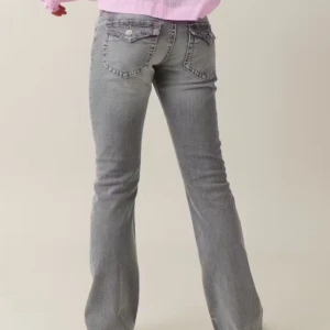 Grå bootcut jeansbyxor med fickdetaljer - Säljer ett par grå jeansbyxor med bootcut-passform och snygga fickdetaljer med knappar bak. Jeansen har normal passning och klassisk femficksdesign. Perfekta för dig som gillar en tidlös look med lite extra edge.