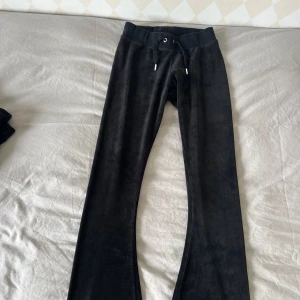 Svarta Juicy Couture med snörning - Svarta mjukisbyxor i mjukt material med resår och snörning i midjan. Byxorna har en diskret broderad logga framtill och bootcut modell. Perfekta för en avslappnad stil.