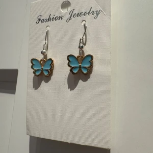 Blå fjärilsörhängen Fashion Jewelry - Superfina örhängen med blå fjärilar och guldfärgade kanter. Hängande modell som ger en söt och lekfull vibe. Perfekta för att addera lite färg och personlighet till din look. Passar dig som gillar detaljer och unika smycken.