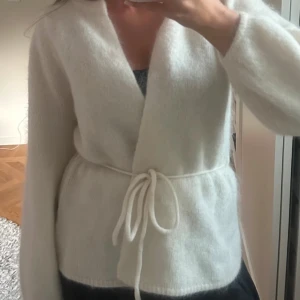 Vit stickad kofta från ella&il - Supermjuk vit kofta från ella&il i omlottmodell med knytband i midjan. Stor i storleken så passar även S. Köpt för 3700kr
