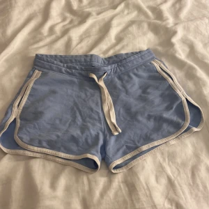 Blå mjuka shorts  - Snygga ljusblå shorts med vit kant och snörning i midjan. De är tillverkade i mjuk bomull och har en loose passform som gör dem superbekväma. Perfekta för chill dagar eller träning under sommaren.