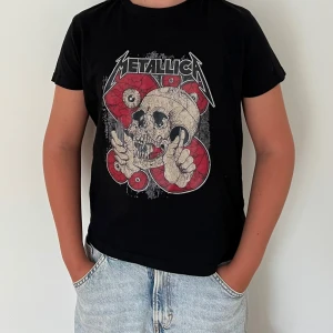 Svart Metallica t-shirt med tryck - Svart t-shirt med Metallica-tryck framtill. Motiv med dödskalle och röda ögon, coolt och edgy design. Klassisk passform med rund hals och korta ärmar. Perfekt för dig som gillar rock och vill sticka ut med en snygg bandtröja.