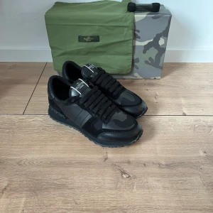 Valentino Garavani Rockrunner sneakers - Svarta Valentino Garavani Rockrunner sneakers med coola camouflage-detaljer. Skorna har en mix av skinn och mocka, grov sula och klassisk snörning. Perfekta för dig som vill ha en lyxig och edgy look med streetkänsla.