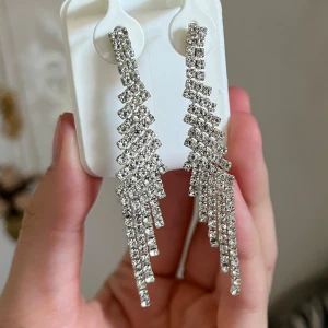 Glittriga silverfärgade örhängen - Perfekt för nyår eller fest - Säljer ett par långa, glittriga örhängen  med flera rader av gnistrande stenar som hänger i en cool, geometrisk form. Perfekta för att ge din look extra bling och wow-faktor. Supersnygga till en partyoutfit eller när du vill sticka ut.