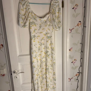 Vit blommig långklänning Gina Tricot - Supersöt långklänning från Gina Tricot i vitt med gula och gröna blommor. Klänningen har puffiga korta ärmar och en lite slits längst ner på vänster sida. Inga skador i sömmar eller tyg och är knappt använd.