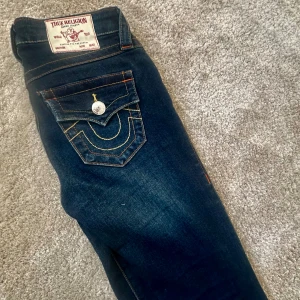 True Religion mörkblå jeans med kontrastsömmar - Snygga mörkblå jeans från True Religion med kontrastsömmar och stora bakfickor med silverfärgade knappar. Säljs pga att dem inte kommer till användning. Hör av dig vid frågor!🥰