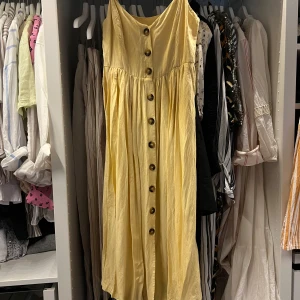 Gul sommarklänning från H&M - Säljer en ljusgul klänning från H&M i storlek 34. Klänningen har knappar framtill, smala axelband och en luftig, avslappnad passform + fickor!. Perfekt för varma dagar och har en mjuk känsla mot huden. Stilren och enkel design som är lätt att matcha.