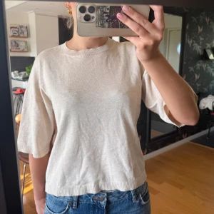 Beige stickad tröja från Soft Rebels - Säljer en beige stickad tröja från Soft Rebels med rund hals och korta ärmar. Tröjan har en enkel och clean look med ribbade detaljer vid hals och nederkant. Perfekt för dig som gillar stilrena och mjuka plagg.