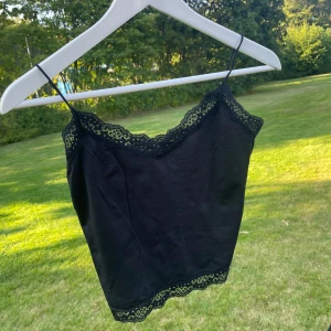 Svart croppad linnetopp från ONLY - Snygg svart croppad linnetopp från ONLY med tunna axelband och spetsdetaljer längs halsringning och nederkant. Perfekt för lager på lager eller till ett par höga jeans. Toppens material är mjukt och stretchigt för en bekväm passform. Passar storlek S jättebra